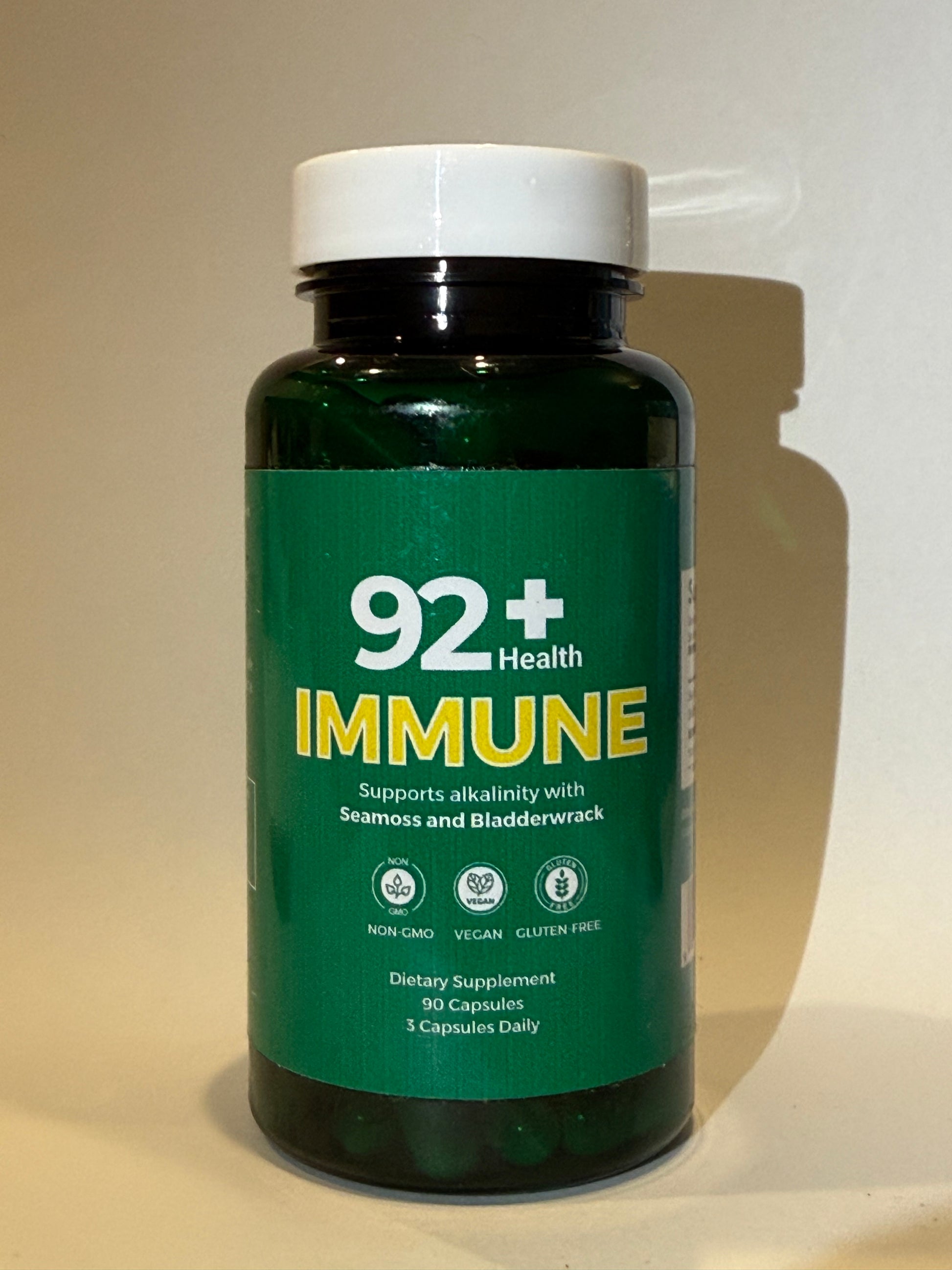 92+ Immune Sea Moss Capsules bottle on wooden surface with yellow background