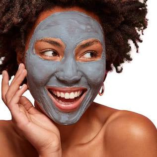 Smiling woman with food grade bentonite clay face mask applied, showcasing clear and healthy skin benefits.